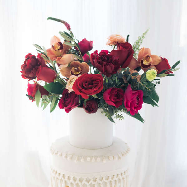 Red and peach floral arrangement in a white vase on a stool