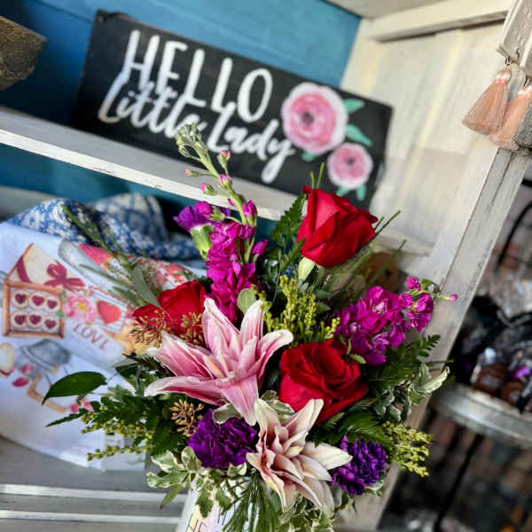 Bouquet of red roses, pink lilies, and purple flowers in a white mug vase