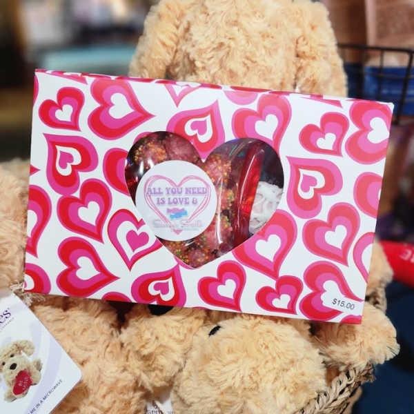 Teddy bear holding a heart-patterned gift box with candy inside