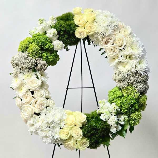 Circular floral wreath of white and green flowers on a black stand