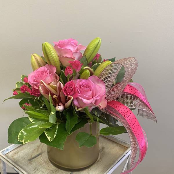 Pink roses and lilies arranged in a gold vase with a pink ribbon