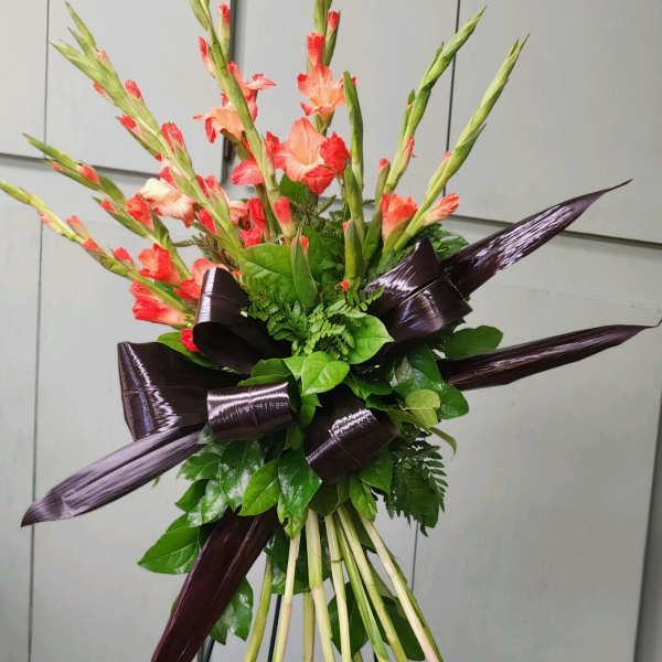 Tall bouquet of coral gladiolus with dark ribbon accents
