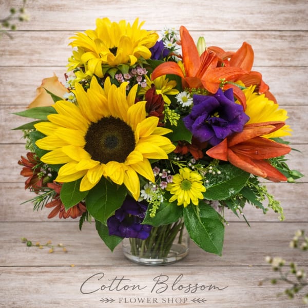 Bright mixed bouquet with sunflowers, orange lilies, and purple blooms in a glass vase