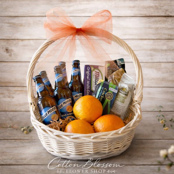 Gift basket with beer bottles, oranges, and snacks in a white wicker basket