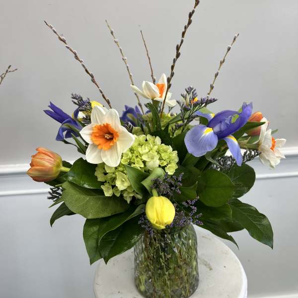 Springy mixed bouquet with daffodils, tulips, irises, and green hydrangea in a green glass vase