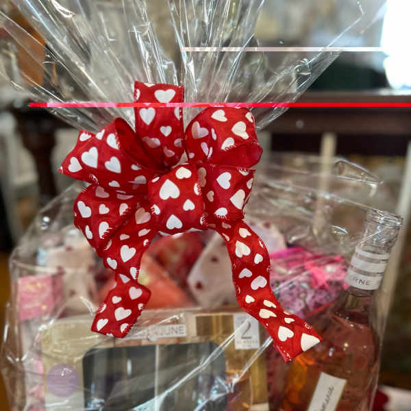 A gift basket wrapped in clear cellophane with a red heart ribbon and wine bottle.