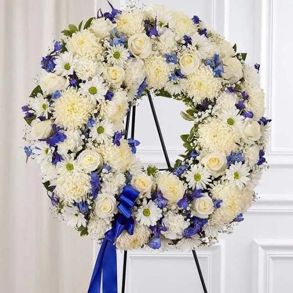 White and blue floral wreath on a black stand with a blue ribbon