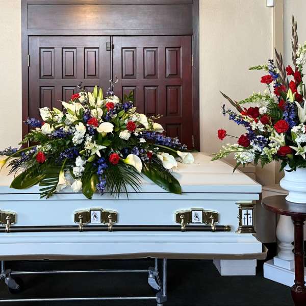 White casket with red, white, and blue funeral flower sprays