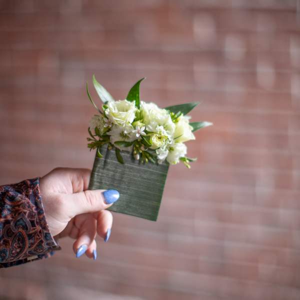 Small white floral corsage with green leaves on a wrist