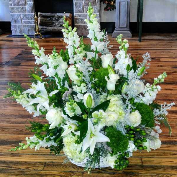 Large white arrangement with lilies, roses, snapdragons and hydrangeas in a basket with silver foliage.