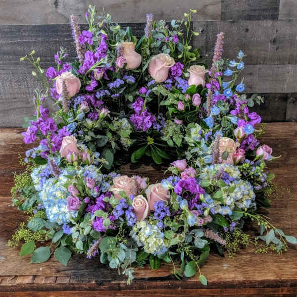 Pastel wreath of pink roses and purple and blue blooms arranged in a ring.