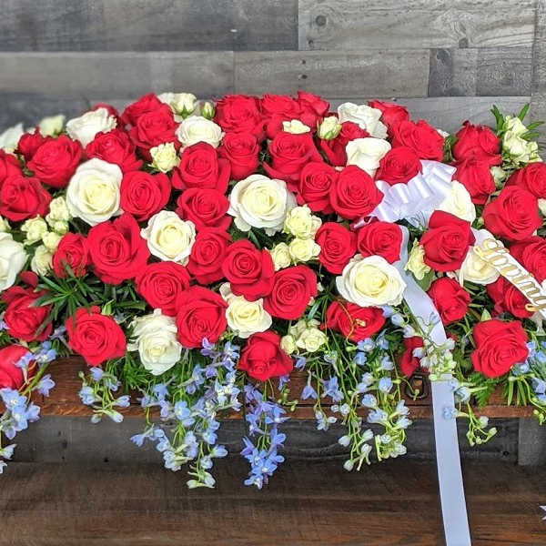 Large red and white rose casket spray with trailing light blue flowers and white ribbon