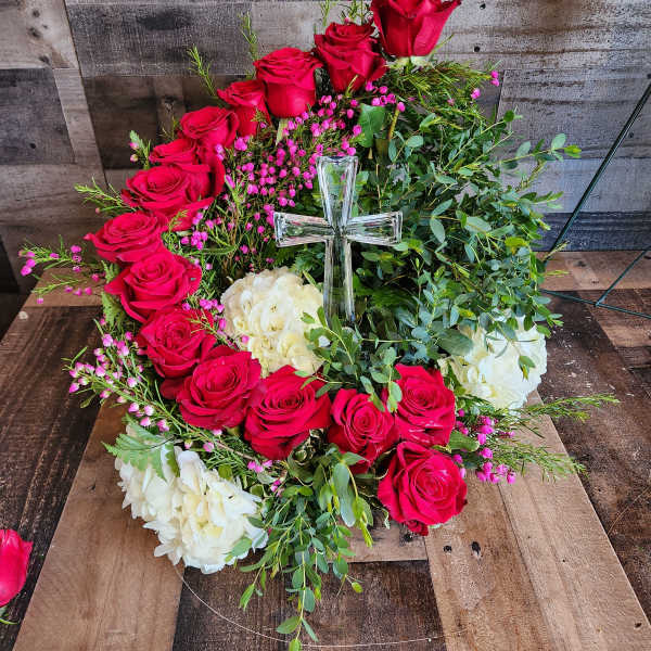 Circular wreath of red roses and white hydrangeas with a clear glass cross in the center