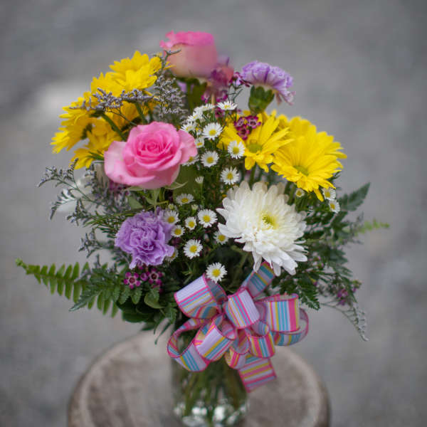 Mixed bouquet of pink, yellow, white, and purple flowers in a glass vase