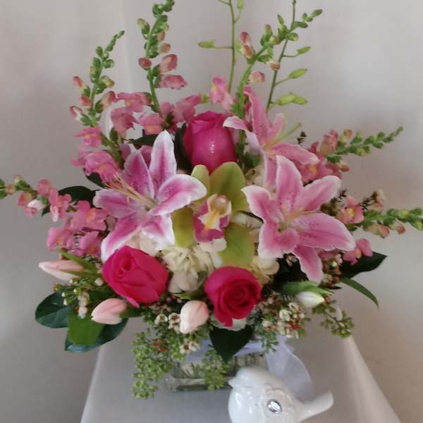 Pink lilies and roses arranged in a glass vase with a small white bird figurine
