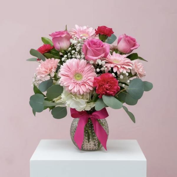 Pink roses and gerbera daisies in a glass vase with a ribbon