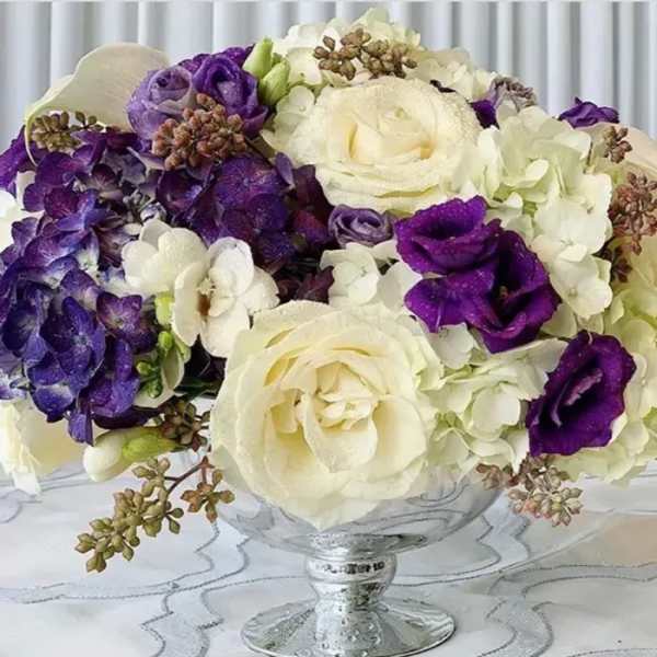 Purple and white floral bouquet in a clear glass pedestal vase