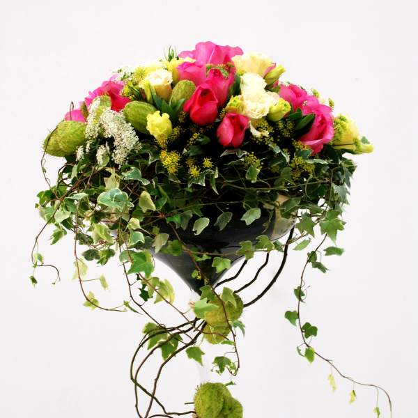 Pink and yellow rose arrangement in a glass vase with trailing ivy