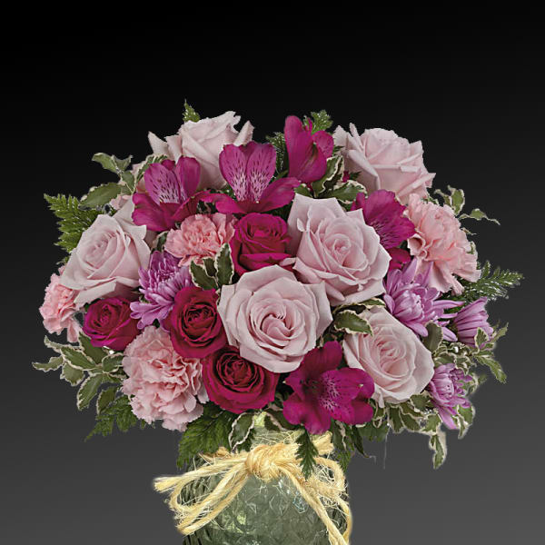 Pink and magenta flower arrangement in a green glass vase with a ribbon bow