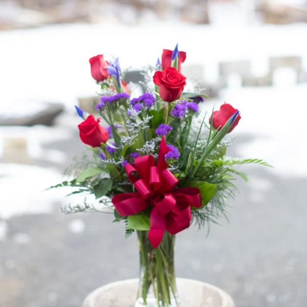 Bouquet of red roses and purple flowers in a clear glass vase