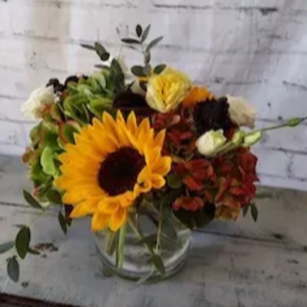Sunflower and mixed autumn flowers in a clear glass vase