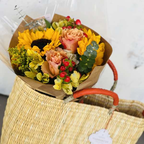 Bouquet of sunflowers, peach roses, and yellow flowers in brown paper