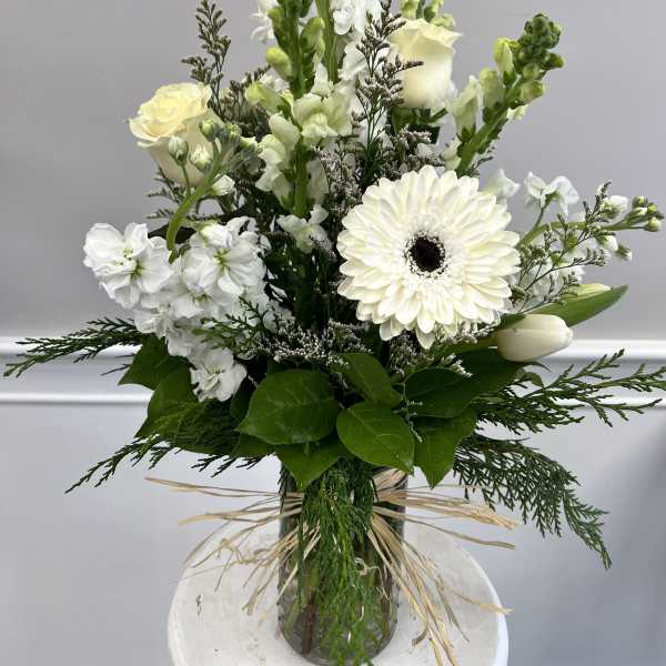 Tall white arrangement with roses, gerbera daisy, snapdragons, and tulips in a clear glass vase tied with raffia.