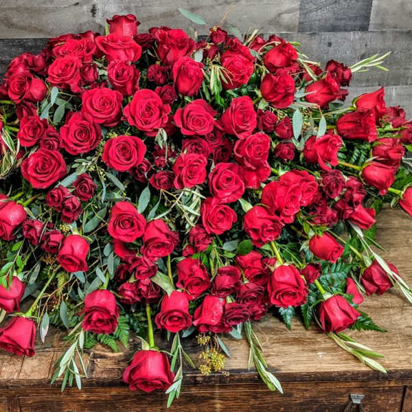 Large mound of red roses arranged in a low cascading display on a wooden surface