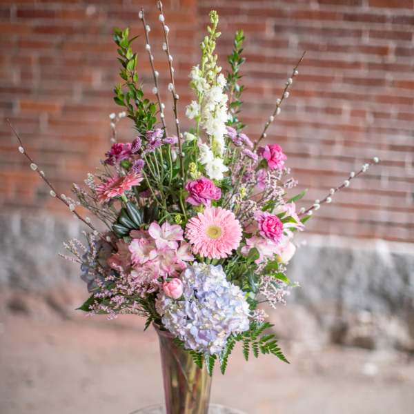 Tall pastel bouquet in a clear glass vase on a stool