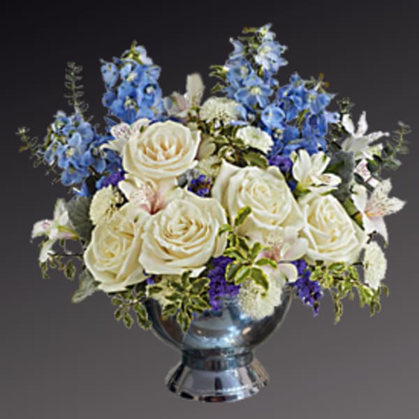 White roses and blue flowers arranged in a silver vase