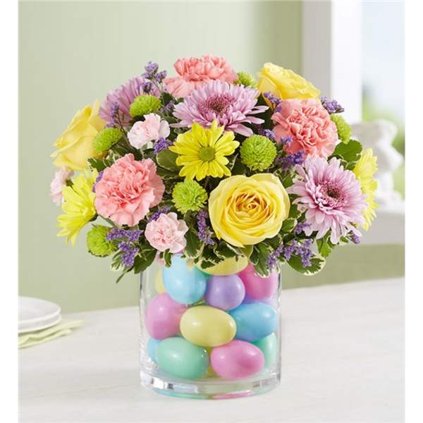 Bouquet of pastel flowers in a glass vase filled with colorful eggs
