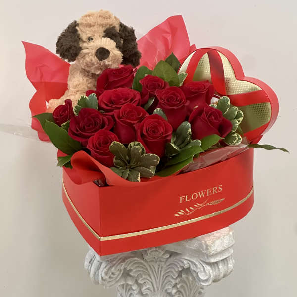 Red roses in a heart-shaped box with a plush dog