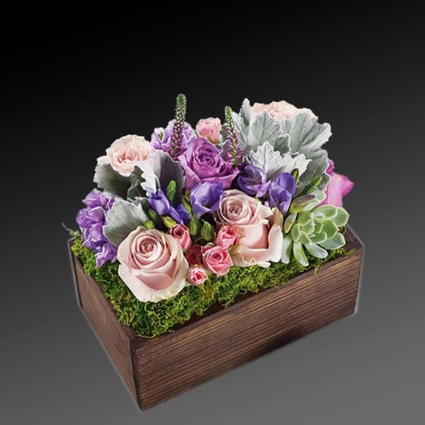Pink and purple floral arrangement in a wooden box with moss