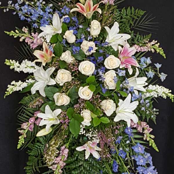 Standing funeral spray with white lilies, roses, and blue flowers