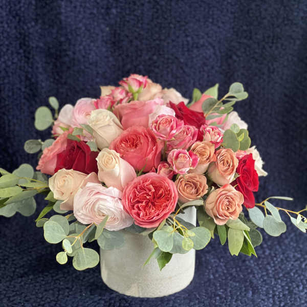Pink and red roses arranged in a white round box with eucalyptus