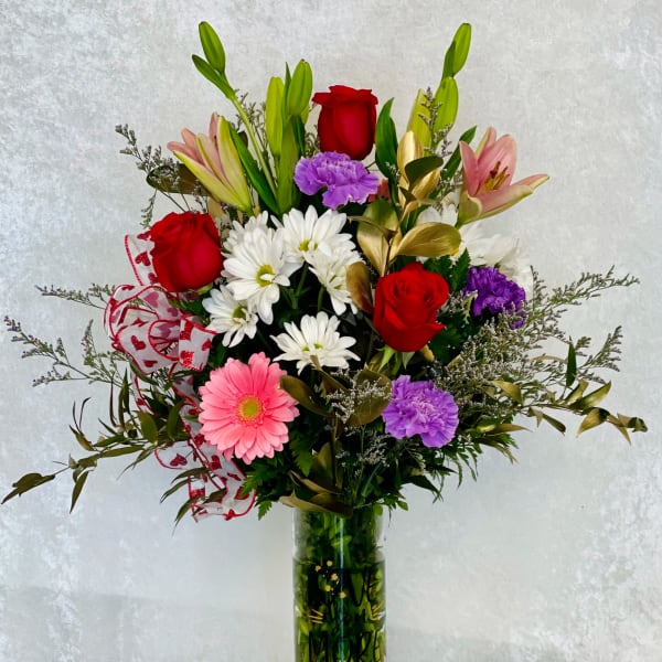 Mixed bouquet of roses, lilies, daisies, and carnations in a glass vase