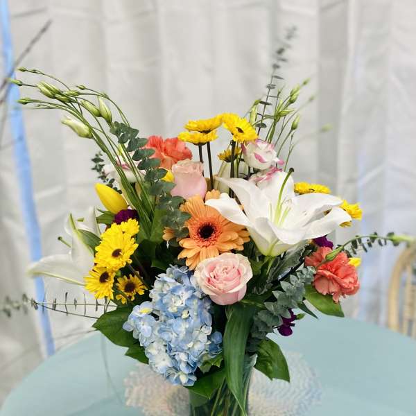 Mixed bouquet in a clear glass vase with lilies, roses, gerbera daisies, and hydrangea