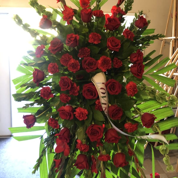Tall standing arrangement of red roses and carnations with palm leaves