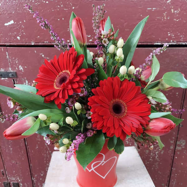 Red gerbera daisies and pink tulips in a red vase