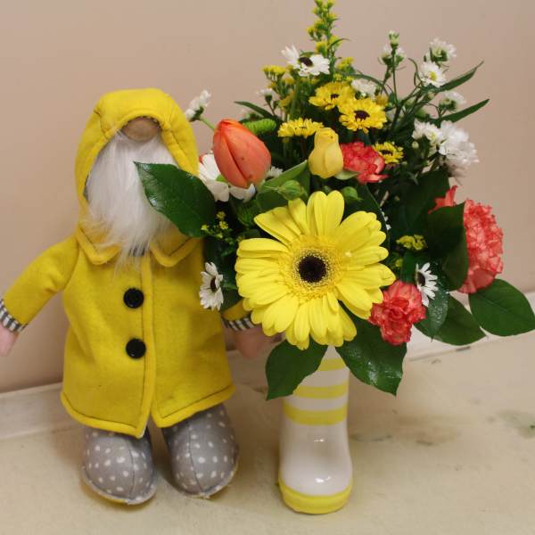 Yellow-clad doll beside a mixed bouquet in a white vase
