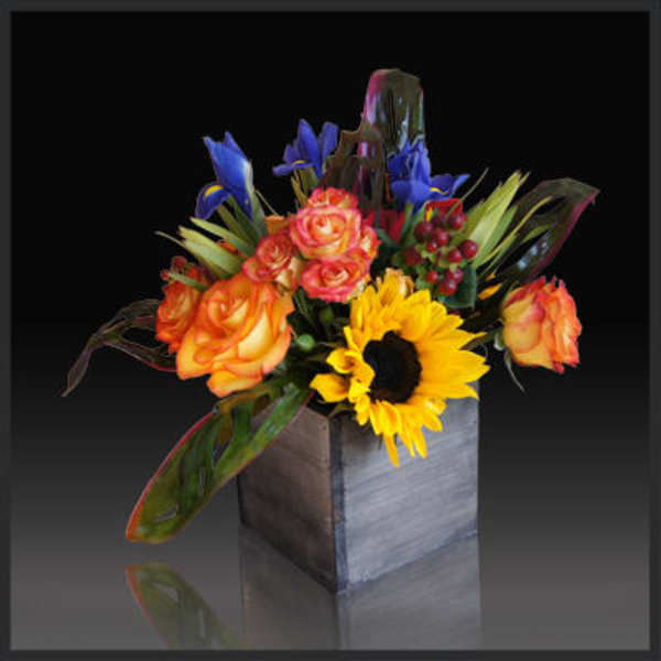 Bouquet of orange roses, blue irises, and a sunflower in a square vase