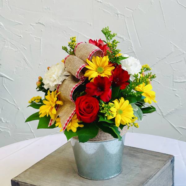 Red and yellow flower arrangement in a metal bucket with burlap ribbon