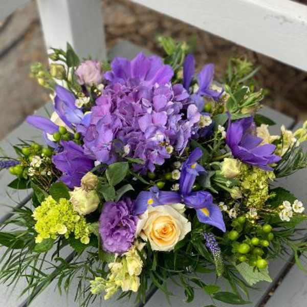 Low arrangement of purple hydrangea, irises, and cream roses with mixed accent blooms