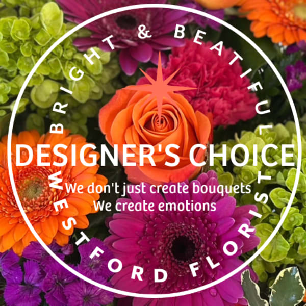 Bright mixed arrangement with orange roses, gerbera daisies, pink and purple blooms, and green hydrangea.