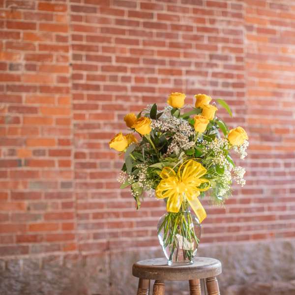 Yellow rose bouquet in a clear glass vase with a yellow ribbon