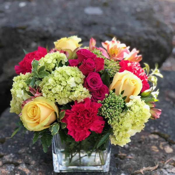 Mixed bouquet of roses, hydrangeas, and carnations in a glass vase