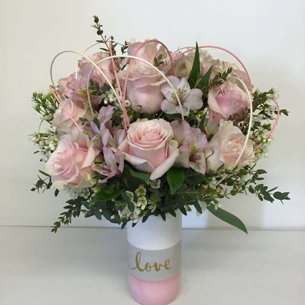 Pink rose bouquet in a white and pink vase with the word love