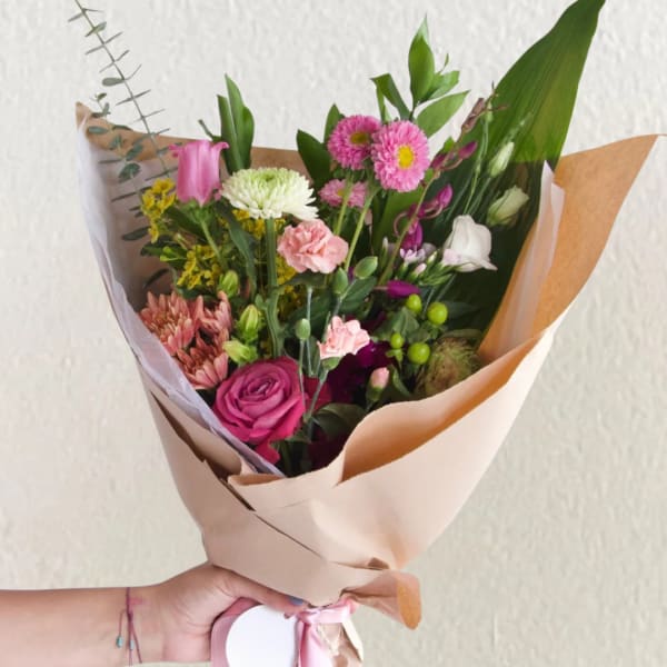 Hand-tied bouquet of pink, white, and yellow flowers wrapped in tan paper