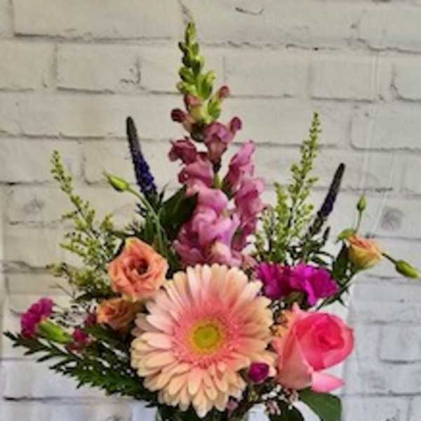 Mixed pink and peach flowers in a glass jar vase with a ribbon