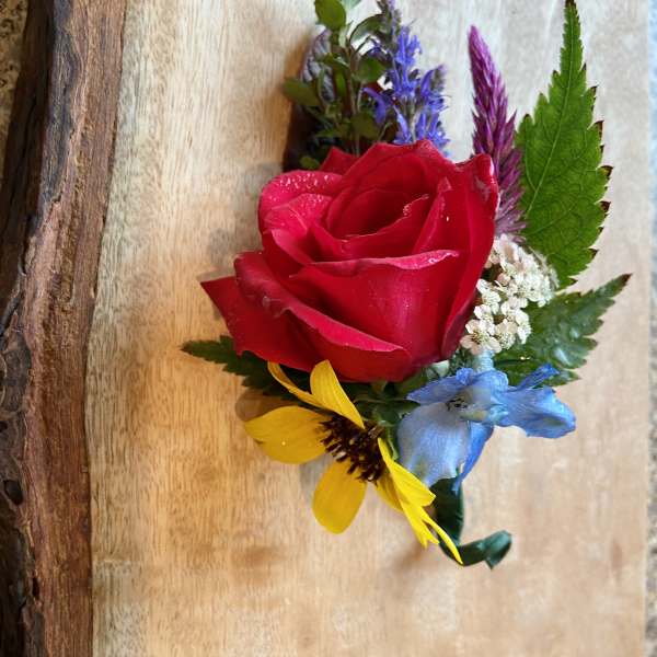 Boutonniere with a red rose and small blue, yellow, and purple flowers